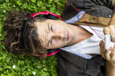 Young handsome man listening music through headphones lying on grass - AFVF08974