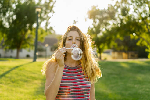 Young woman blowing bubbles standing at park - AFVF08981