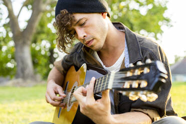 Hübscher junger Mann spielt Gitarre im Park - AFVF08990