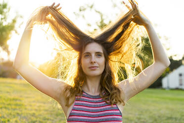 Young beautiful woman looking away with hand in hair standing at park - AFVF08993