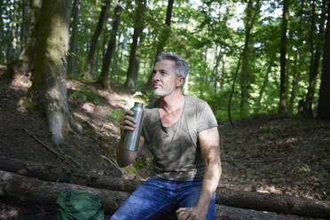 Mann trinkt aus einer Wasserflasche auf einem Baumstamm im Wald sitzend - FMKF07190