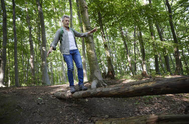 Man balancing while walking on tree trunk at forest - FMKF07194