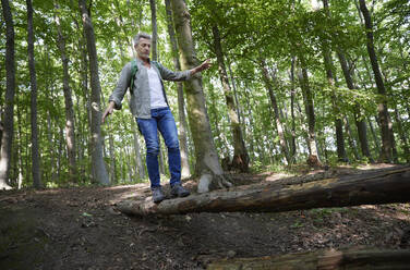 Mann balanciert beim Gehen auf einem Baumstamm im Wald - FMKF07194