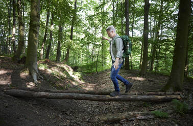 Male backpacker walking with arms outstretched on tree trunk - FMKF07195