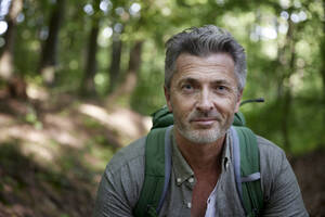 Lächelnder gutaussehender männlicher Wanderer mit Rucksack im Wald - FMKF07198