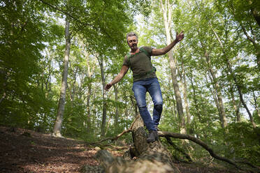 Man with arms outstretched walking on fallen tree in forest - FMKF07203