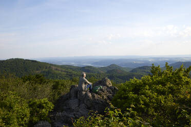 Männlicher Wanderer betrachtet die Landschaft, während er auf einem Berg sitzt - FMKF07205