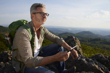 Mann hält digitales Tablet, während er auf einem Berg sitzt - FMKF07218