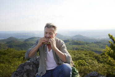 Männlicher Wanderer, der auf einem Berg sitzend etwas isst - FMKF07223