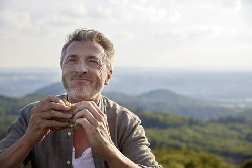 Mann lächelt, während er ein Sandwich hält - FMKF07224