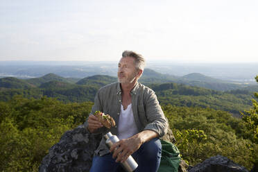 Male hiker with food and bottle sitting on top of mountain - FMKF07225