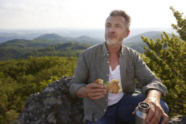 Männlicher Wanderer mit Sandwich und Wasserflasche am Berg - FMKF07226