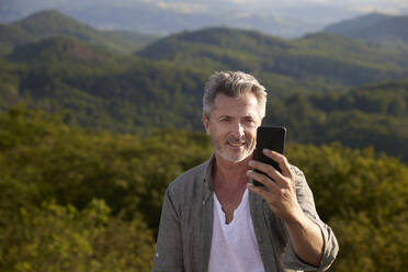 Lächelnder männlicher Wanderer beim Selfie mit dem Smartphone - FMKF07229