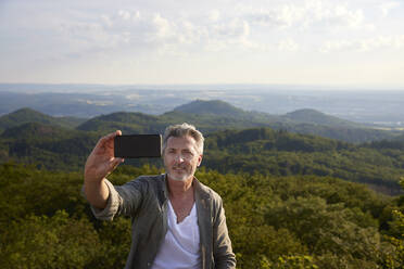 Älterer Mann lächelt, während er ein Selfie mit seinem Mobiltelefon macht - FMKF07231