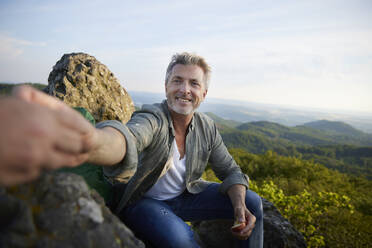 Smiling man giving apple to female friend while sitting on mountain - FMKF07240