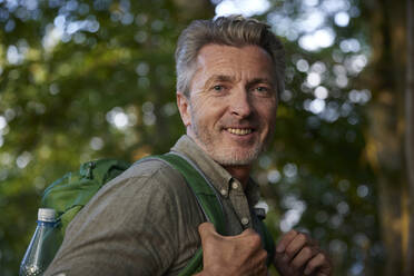 Lächelnder männlicher Wanderer mit Rucksack im Wald - FMKF07261