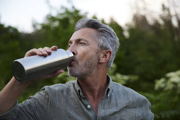 Male hiker drinking water from bottle in forest - FMKF07264