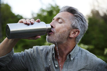 Durstiger Mann verschüttet beim Trinken von Wasser aus einer Flasche im Wald - FMKF07265