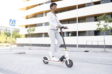 Businesswoman riding electric push scooter on footpath in city - JCCMF02908