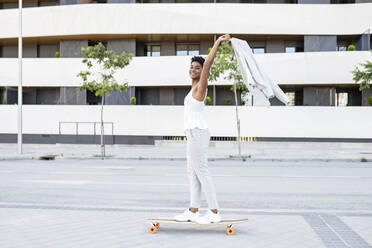 Carefree businesswoman holding blazer while skateboarding in city - JCCMF02912