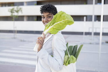 Smiling businesswoman holding leaf vegetable in city - JCCMF02921