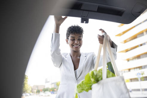 Weibliche Fachkraft lädt Lebensmittel in den Kofferraum eines Autos - JCCMF02924