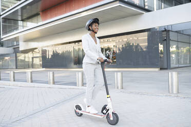 Businesswoman riding electric push scooter near office building - JCCMF02931