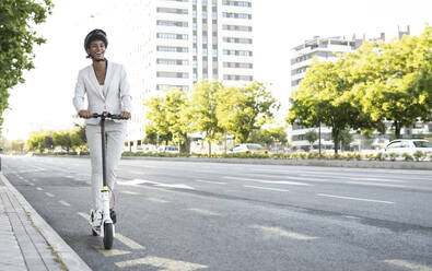 Happy female commuter riding electric push scooter on street in city - JCCMF02932