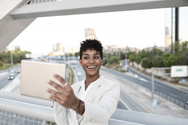 Businesswoman taking selfie through digital tablet on bridge in city - JCCMF02940