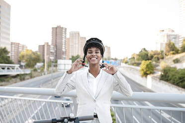 Glückliche weibliche Fachkraft, die einen Helm trägt, während sie auf einer Brücke in der Stadt steht - JCCMF02941