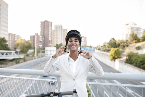 Happy female professional wearing helmet while standing on bridge in city - JCCMF02941