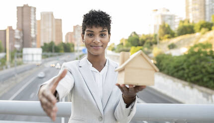 Verkäuferin mit Hausmodell bei der Begrüßung mit Handschlag auf der Brücke - JCCMF02942