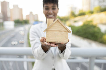 Female real estate agent holding wooden model home - JCCMF02943