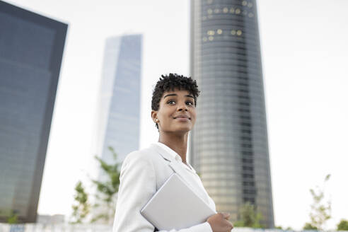 Female business professional looking away holding digital tablet in city - JCCMF02954
