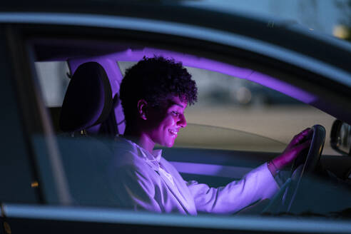 Smiling businesswoman sitting in illuminated purple car at night - JCCMF02963