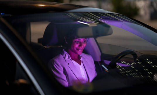 Lächelnde weibliche Fachkraft sitzt nachts im Auto - JCCMF02965