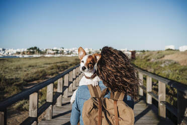 Backpacker holding dog on footpath during sunny day - EBBF04081