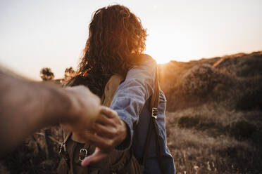 Freundin mit Rucksack hält Hand des Freundes bei Sonnenuntergang - EBBF04086