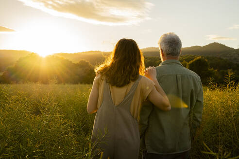 Daughter and father looking at sunset view while standing at in field - AFVF09016