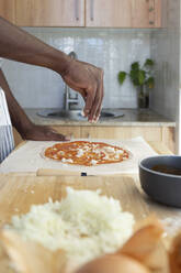 Man topping pizza with chopped onions in kitchen at home - JPTF00862