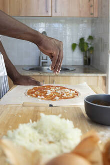 Mann belegt Pizza mit gehackten Zwiebeln in der Küche zu Hause - JPTF00862