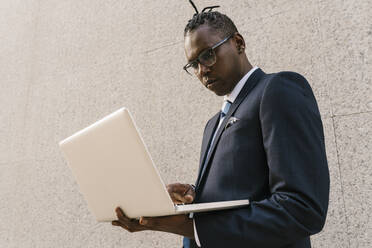 Businessman using laptop while standing in front of wall - EGAF02408