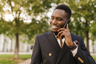 Smiling young man talking on smart phone at park - EGAF02418