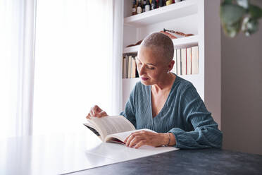 Woman reading book while sitting at home - AGOF00159