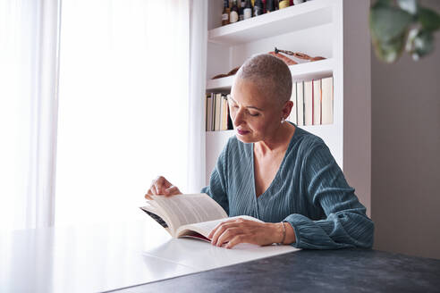 Frau liest ein Buch, während sie zu Hause sitzt - AGOF00159