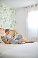 Frau benutzt Smartphone im Schlafzimmer zu Hause - AGOF00168