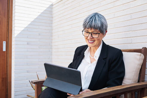 Mature businesswoman with short gray hair using digital tablet in backyard - AGOF00174