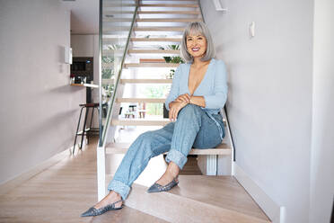 Smiling mature woman sitting on staircase at home - AGOF00183