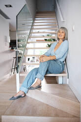 Woman leaning on wall while sitting at staircase - AGOF00184