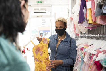 Lesbische Frau mit Gesichtsschutzmaske zeigt ihrer Freundin im Geschäft ihr Kleid - PMF01881